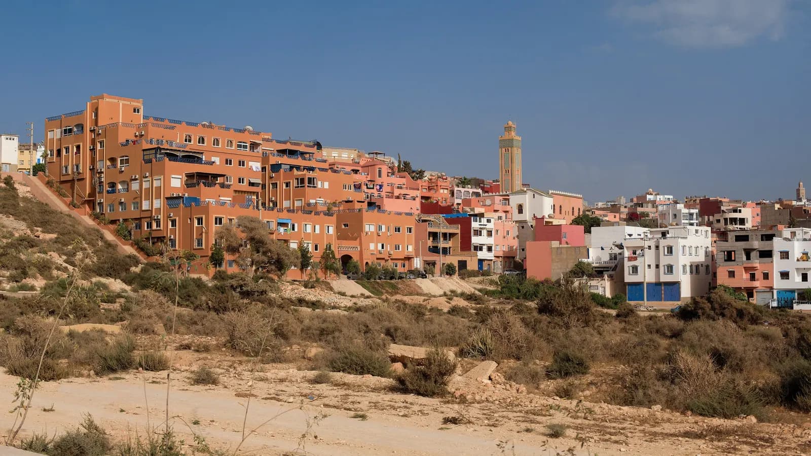 Ochre and white houses of Tamraght climbing a hillside above scrub, with a minaret against a blue sky