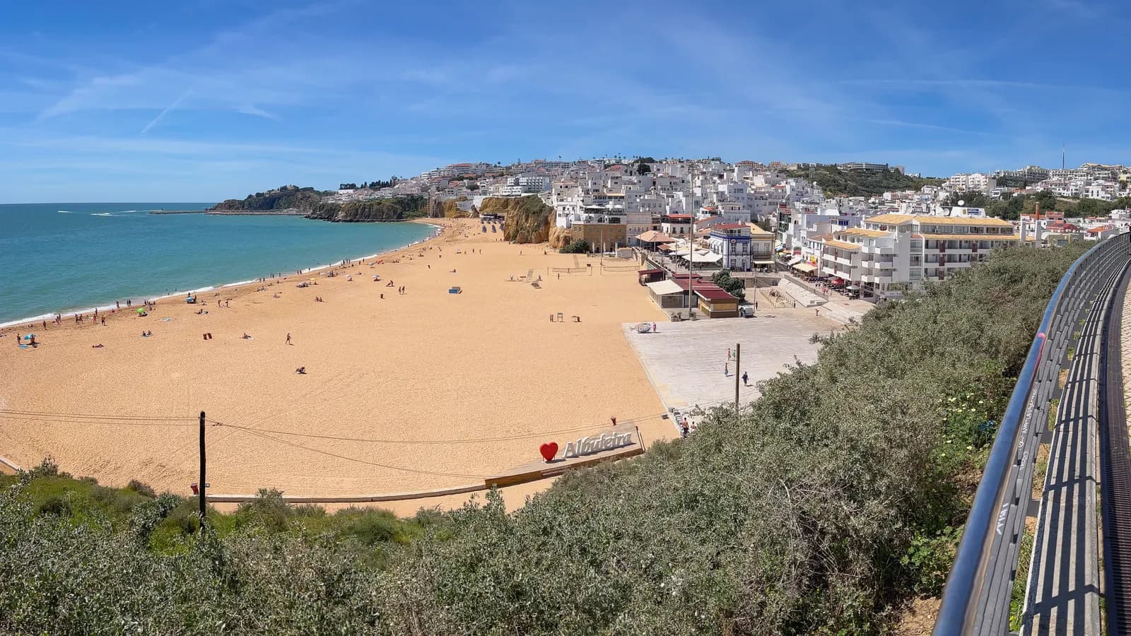 The long beach below Albufeira seen from a clifftop path, with the white houses of the old town on the hill behind