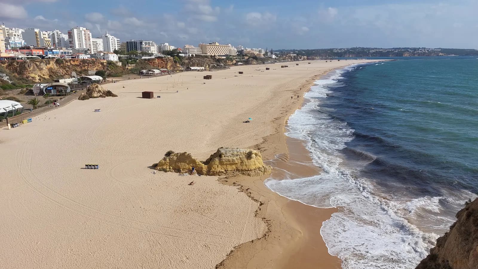 The long sandy Praia da Rocha at Portimão seen from the cliff, with a rock on the beach and hotel towers along the top