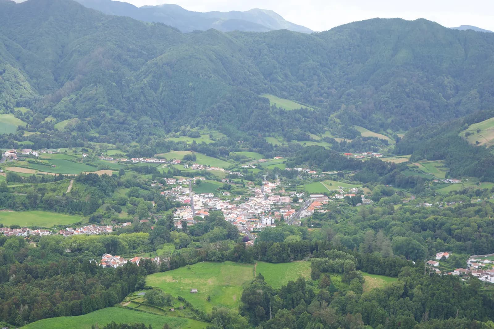 The village of Furnas in a green valley surrounded by forested hills and fields, seen from a viewpoint above