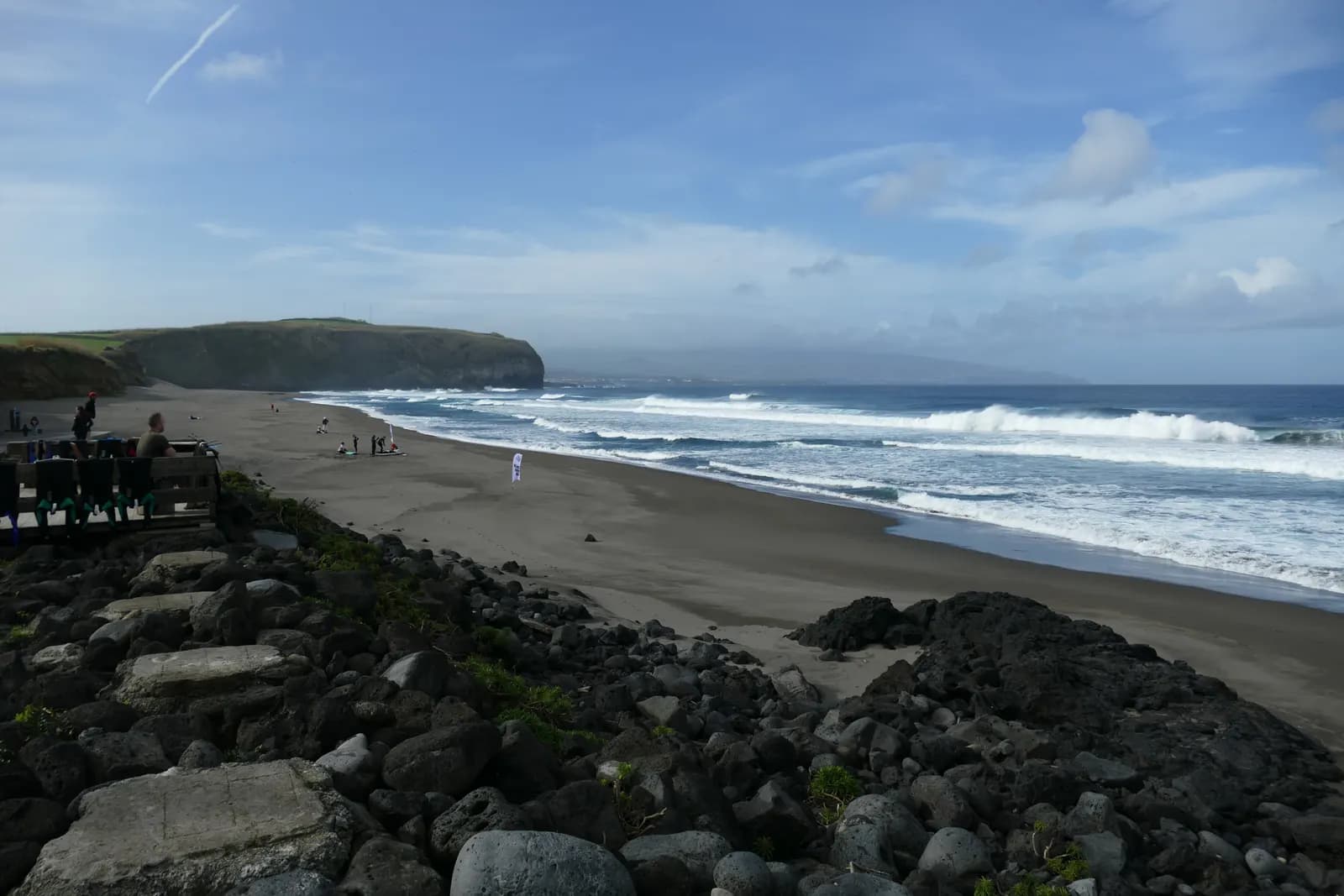 The long dark-sand beach of Santa Bárbara at Ribeira Grande, with breaking waves, a few walkers and a headland in the distance