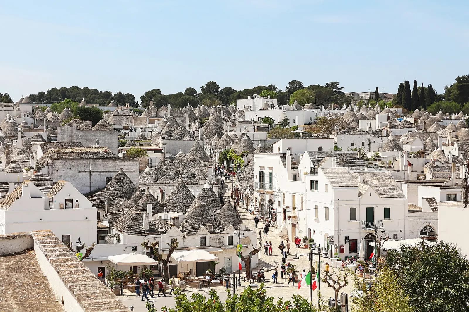 The conical stone roofs of the trulli in the Rione Monti quarter of Alberobello, with a sloping street of whitewashed houses and visitors