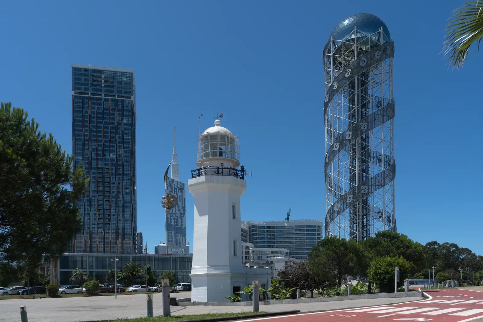 The white Batumi lighthouse on the seafront, with the Alphabetic Tower and high-rise buildings behind