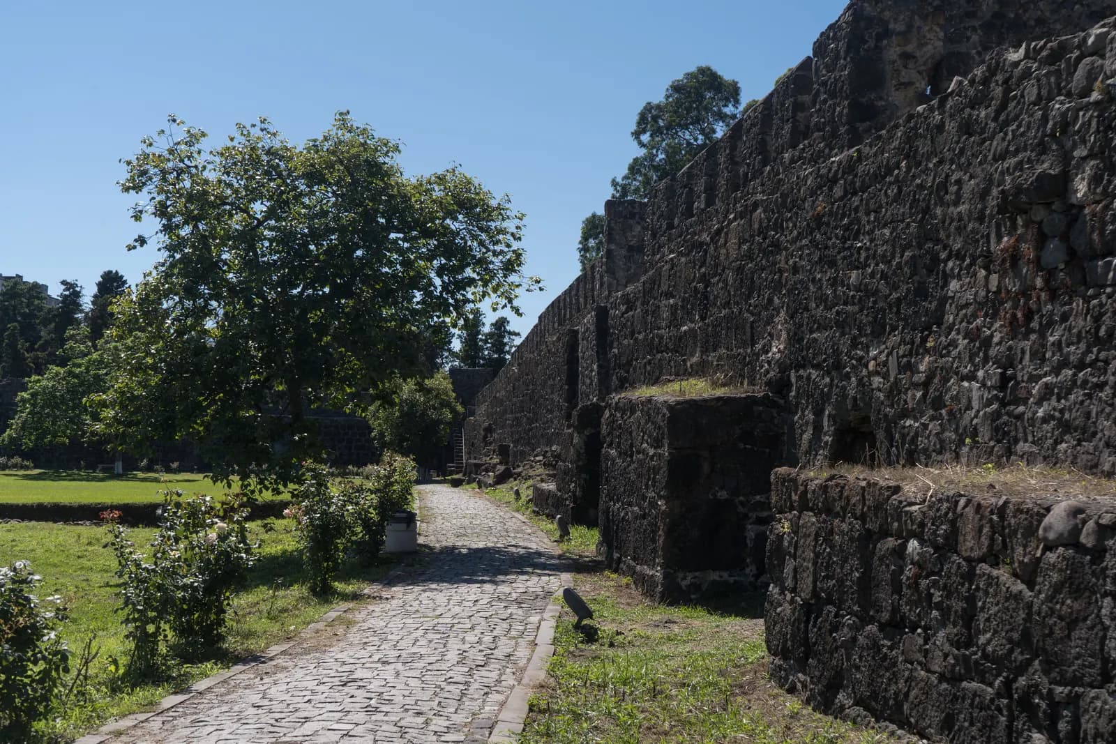 The stone walls of Gonio Fortress with a cobbled path, lawn and trees inside the fort