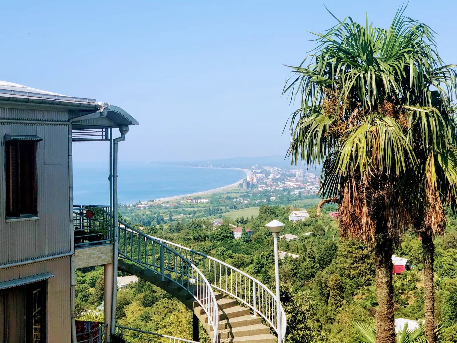 Kobuleti and its long curving beach seen from the hills at Tsikhisdziri, with palm trees and a staircase in the foreground