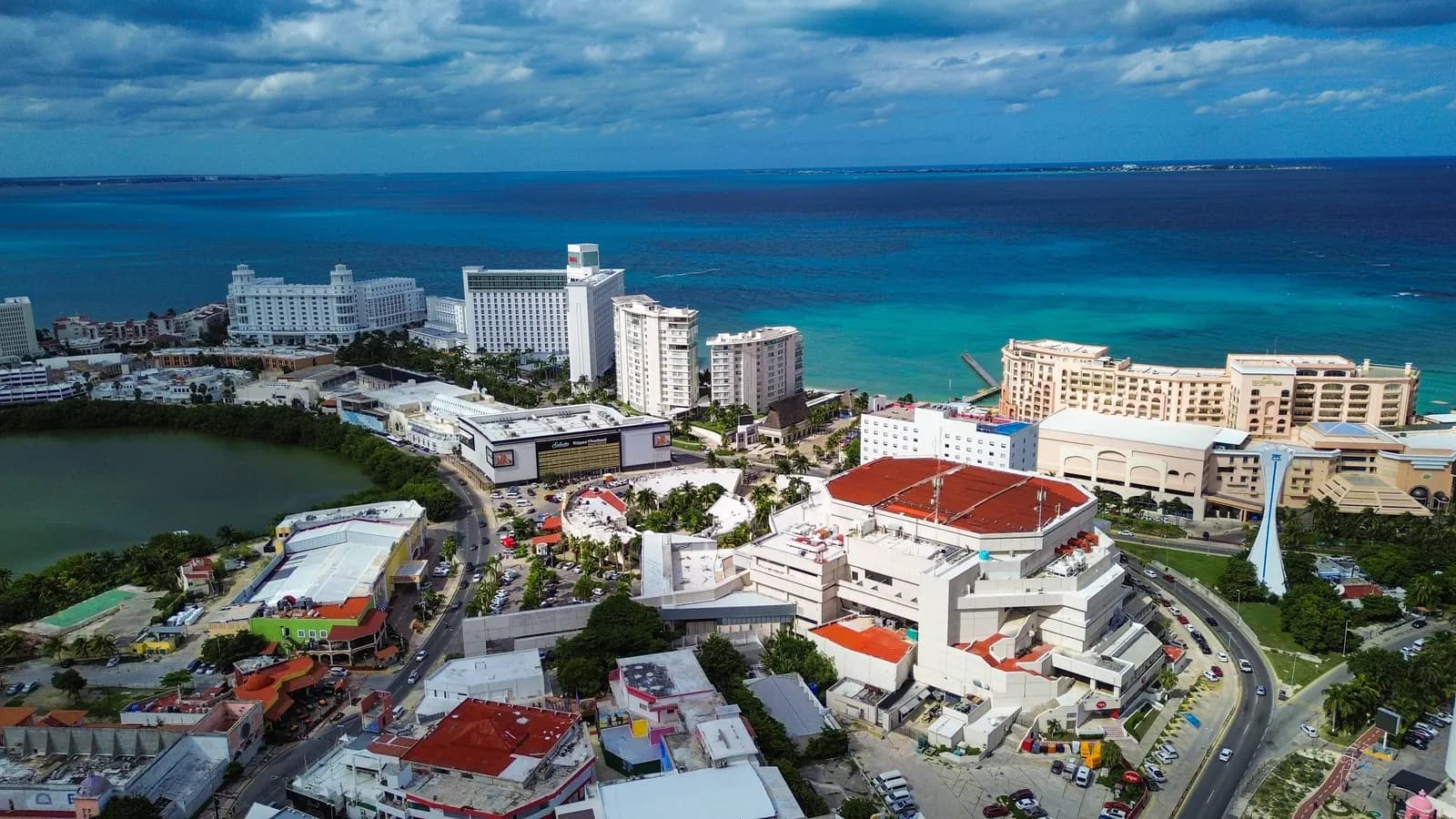 Hotel towers at Punta Cancún seen from the air, with a lagoon on the left, roads and red-roofed buildings in front and the Caribbean Sea behind