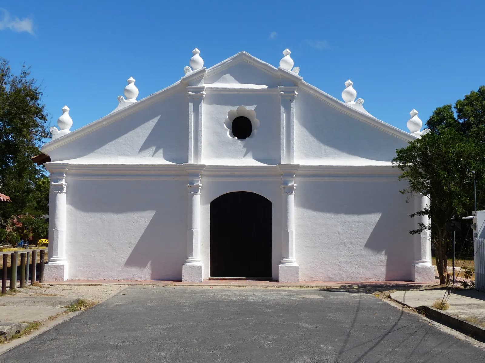 The whitewashed facade of the Ermita de la Agonía church in Liberia, with a dark wooden door, under a clear blue sky