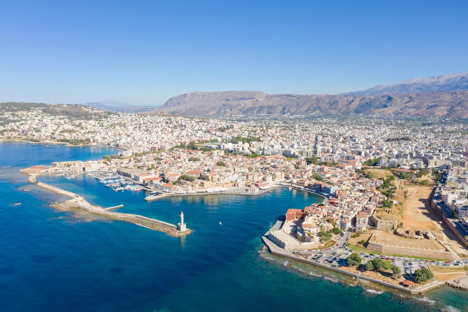 Aerial view of the Venetian harbour of Chania with its lighthouse on the breakwater, the old town behind and the White Mountains in the distance