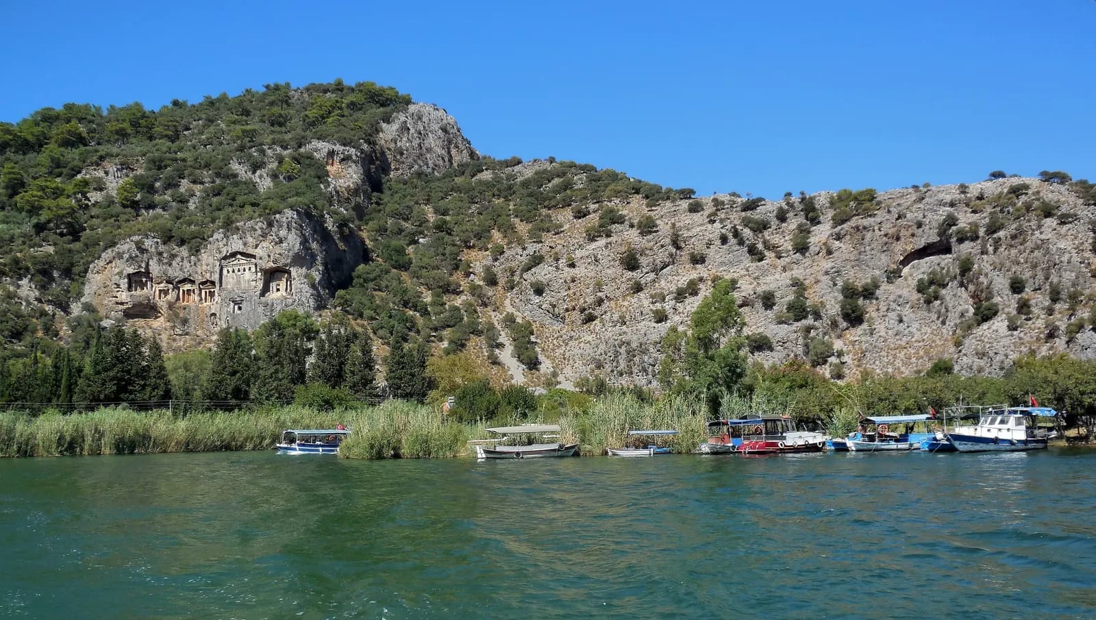 The rock-cut tombs of Kaunos in the cliff above the Dalyan river, with river boats moored along the reeds
