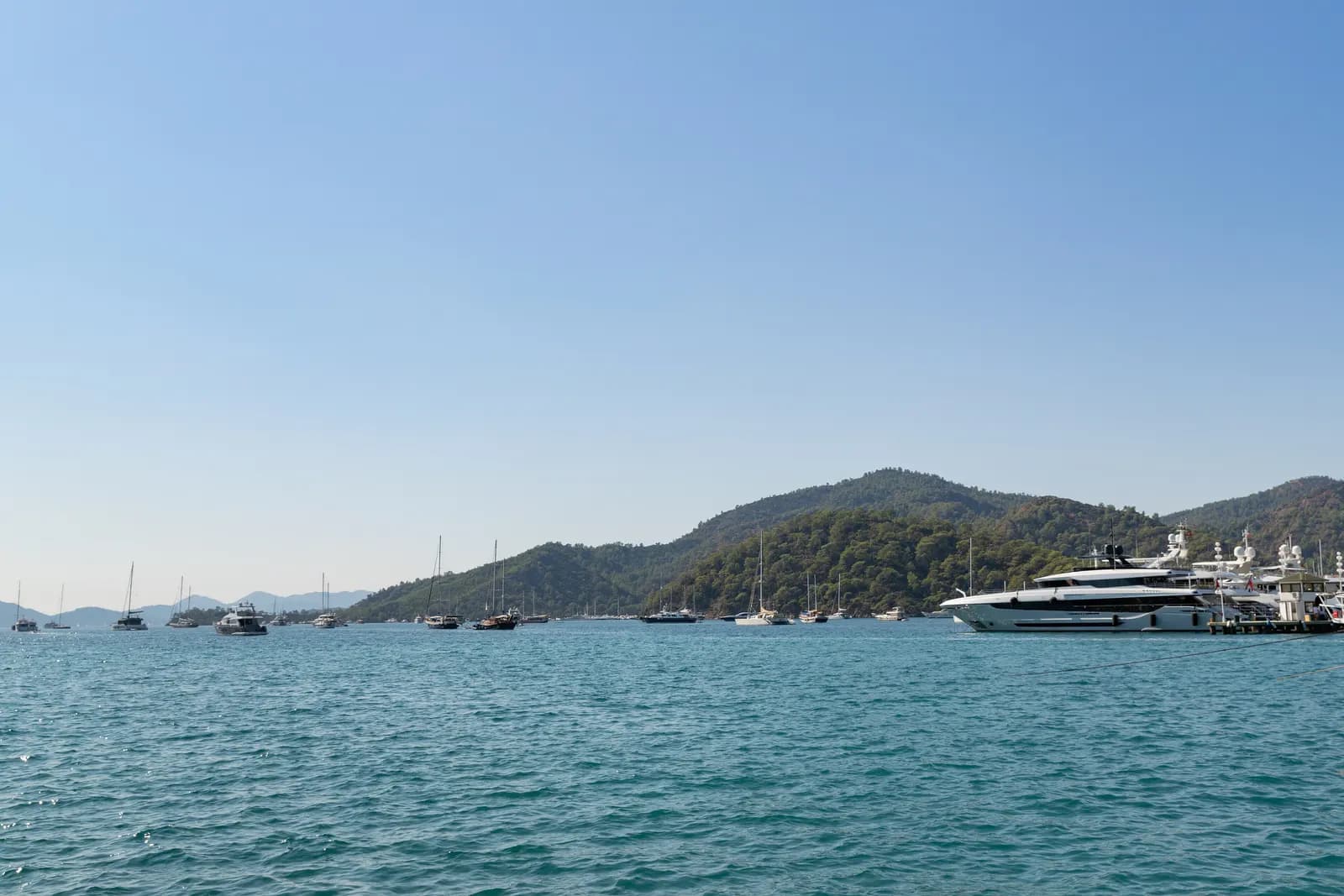 Sailing boats at anchor in Göcek bay and a large motor yacht at the pier, with pine-covered hills behind