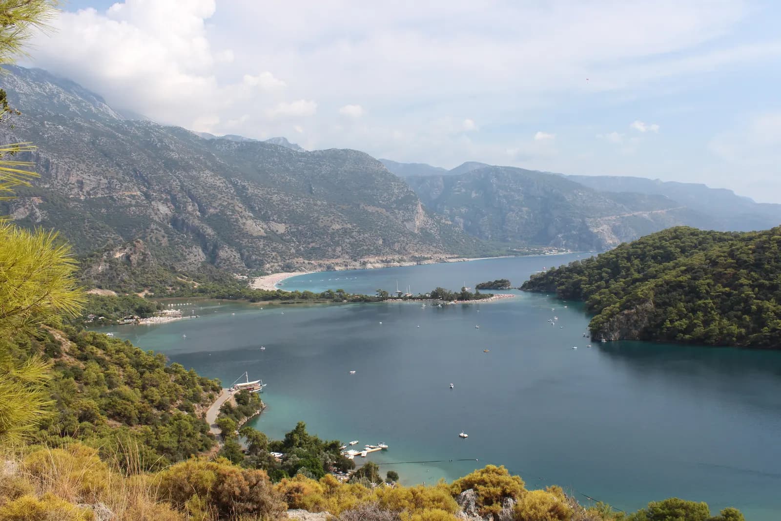 The Ölüdeniz lagoon and the long beach beyond it seen from the pine-covered hill on the path to Kayaköy, with steep mountains along the coast