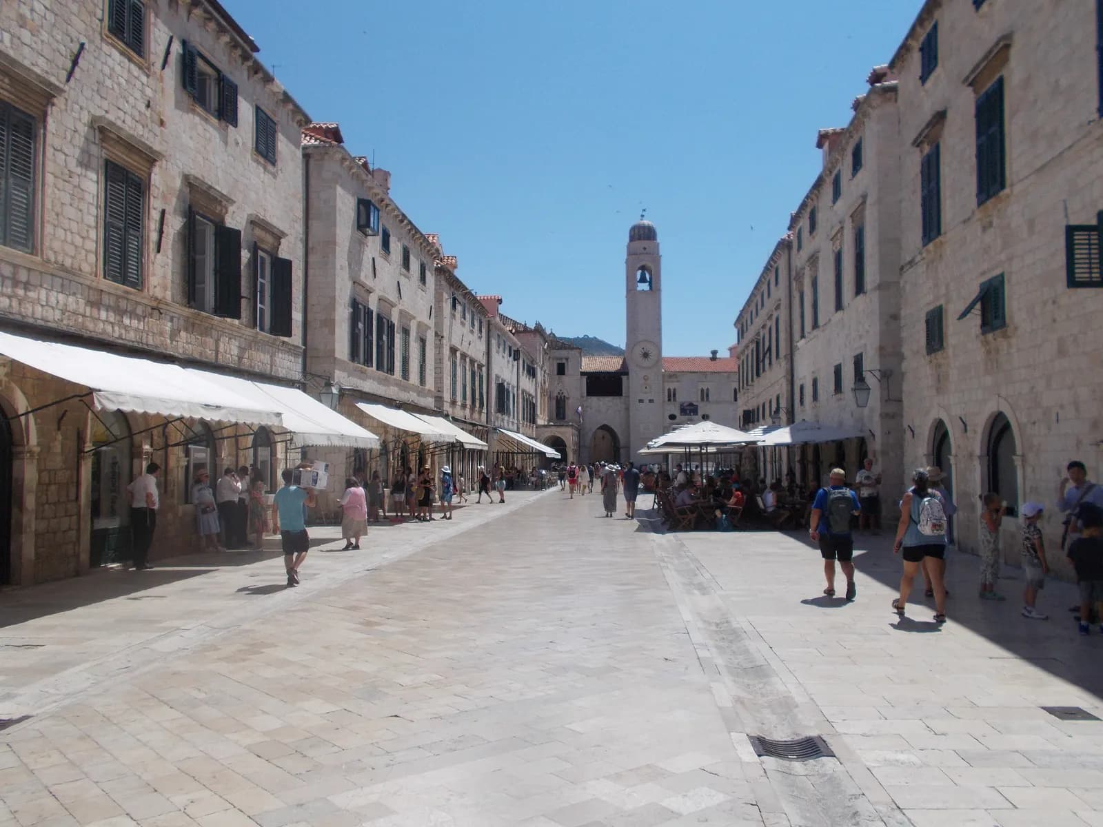 Stradun, the main street of Dubrovnik Old Town, paved in stone and lined with shops, café umbrellas and the clock tower at its end