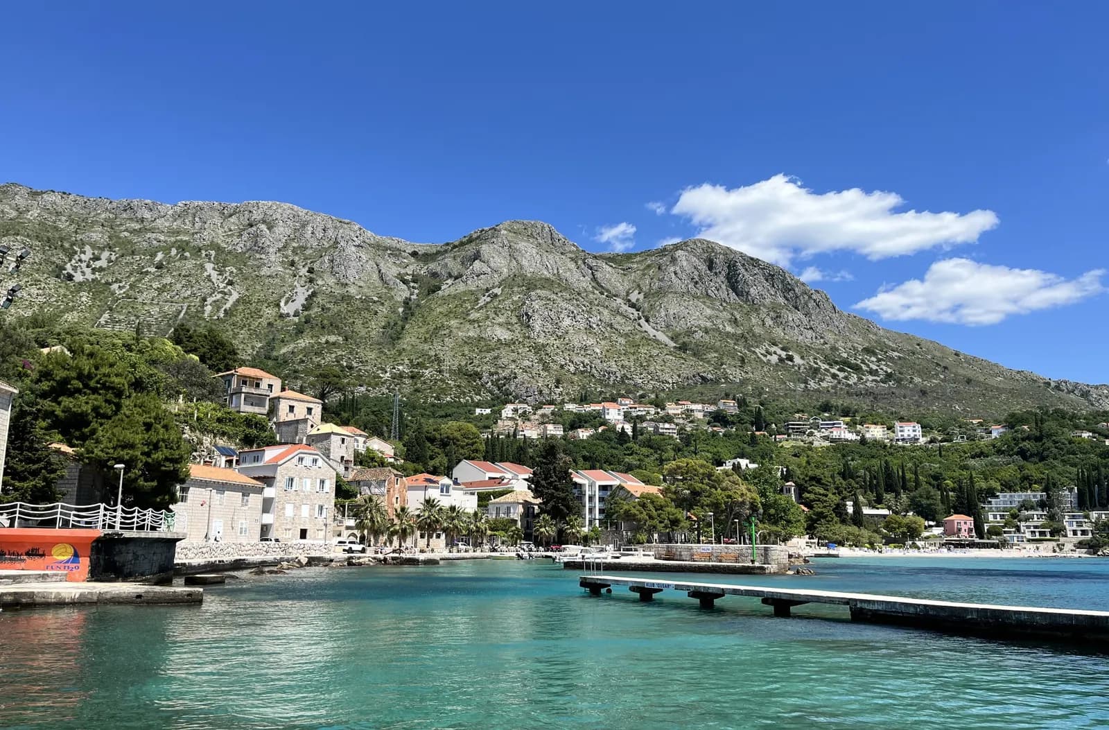 The small harbour at Mlini in Župa dubrovačka, with stone houses, a concrete pier and bare limestone mountains above the coast