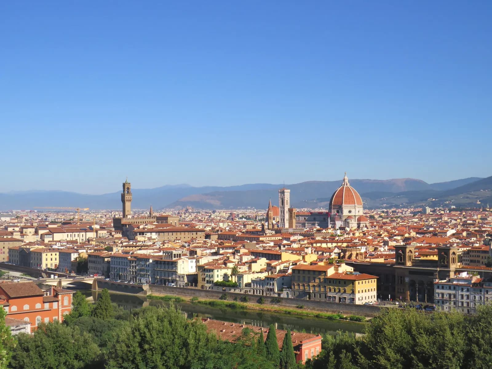 Florence seen from Piazzale Michelangelo on a clear day: the Arno, the Palazzo Vecchio tower and the cathedral dome above the roofs.
