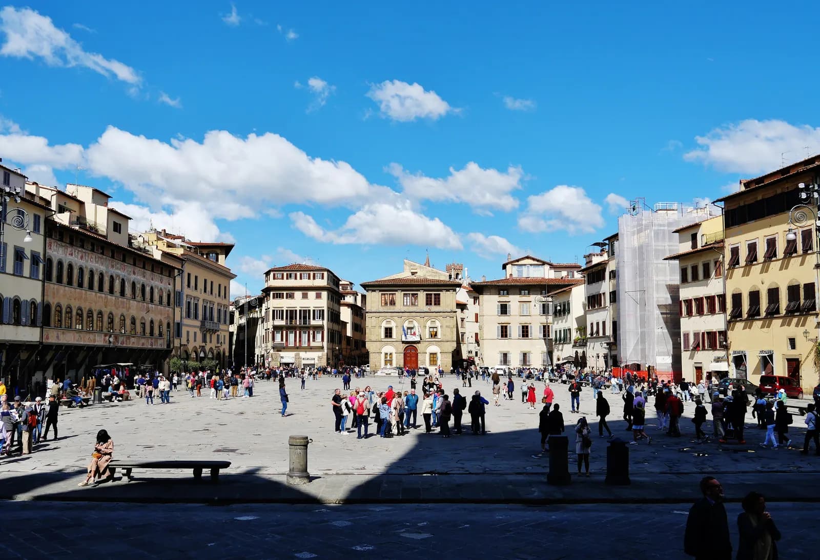 The wide paved Piazza di Santa Croce in spring sunshine, lined with old palazzi, with visitors crossing it.