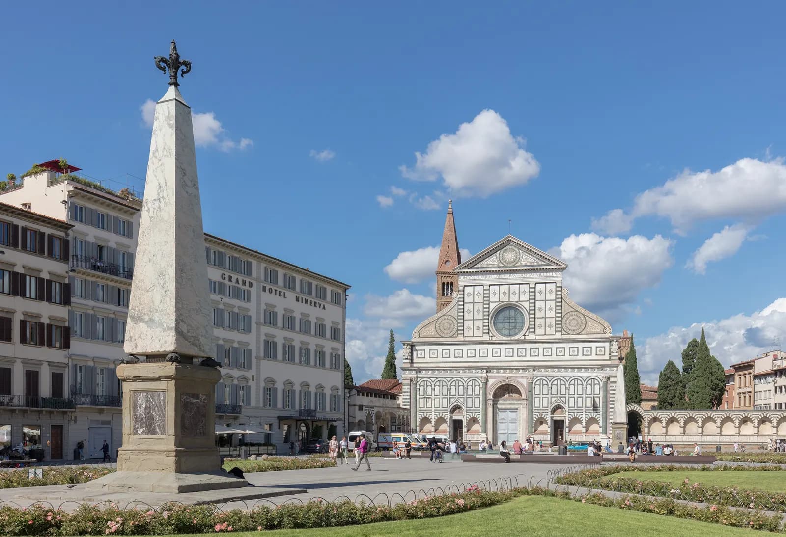 Piazza Santa Maria Novella with a marble obelisk, rose beds and the green and white facade of the basilica.