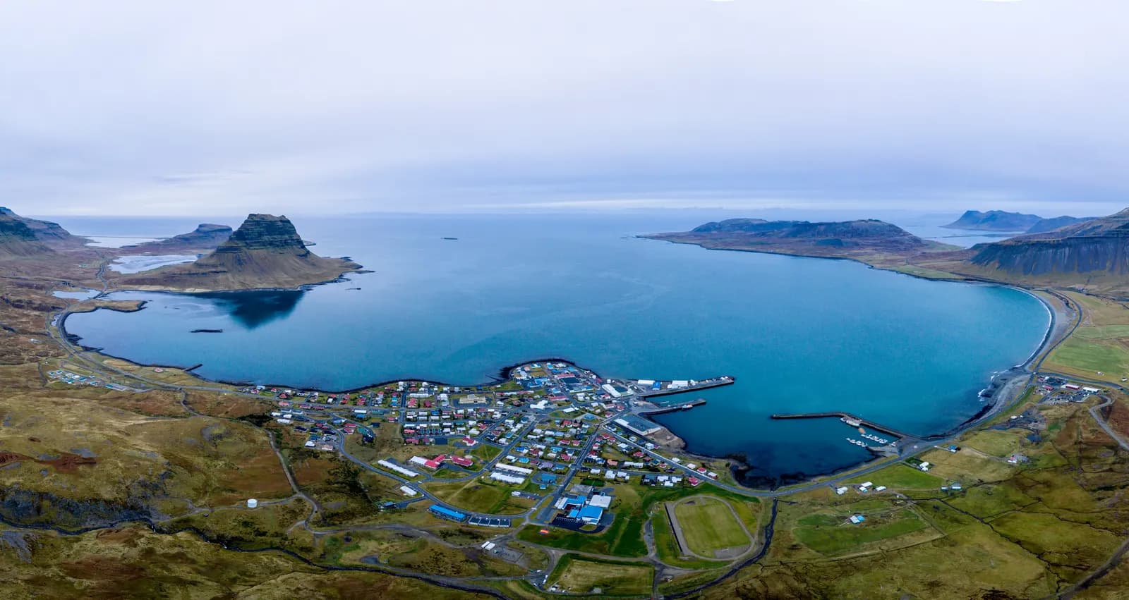 Aerial view of the town of Grundarfjörður on its bay, with the harbour in the middle and the peaked Kirkjufell mountain on the left