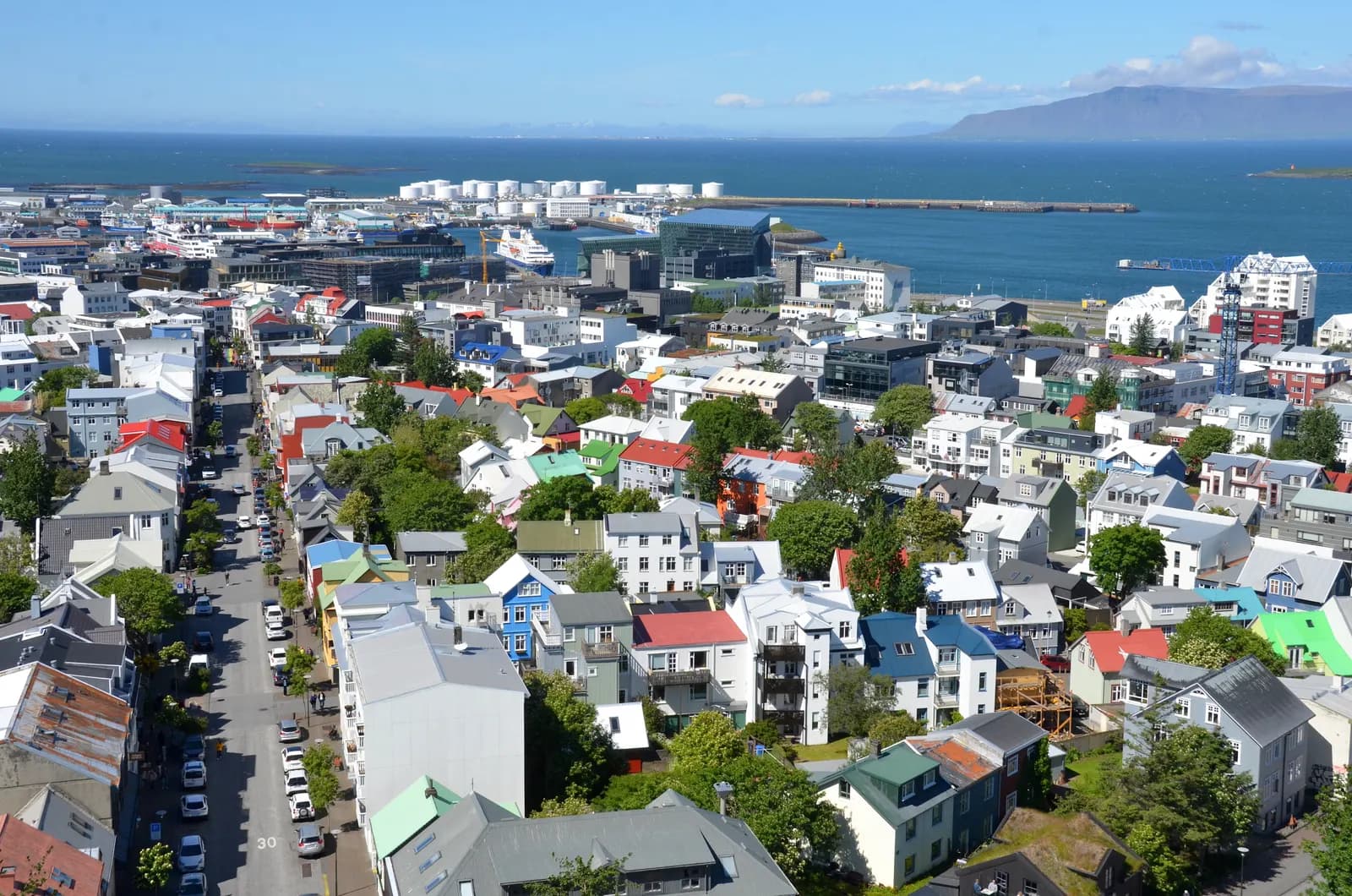 Coloured roofs of central Reykjavík seen from the Hallgrímskirkja tower on a sunny day, with the old harbour, a docked ship and Mount Esja across the bay