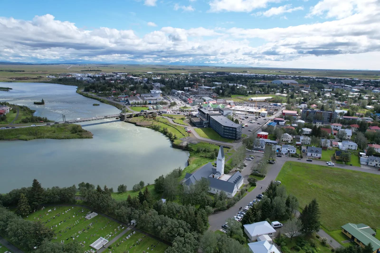 Aerial view of Selfoss beside the Ölfusá river, with the town church in front, the suspension bridge on the left and the town centre behind