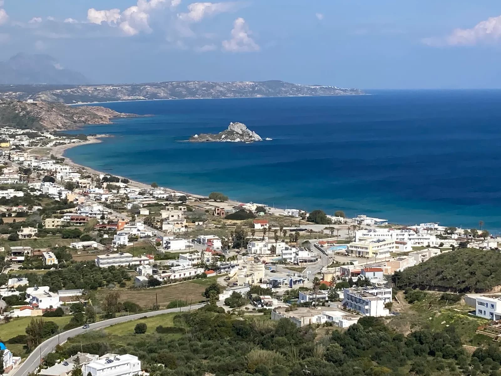 View from the hillside above Kamari over the village and the long beach of Kefalos bay, with the rocky Kastri islet offshore