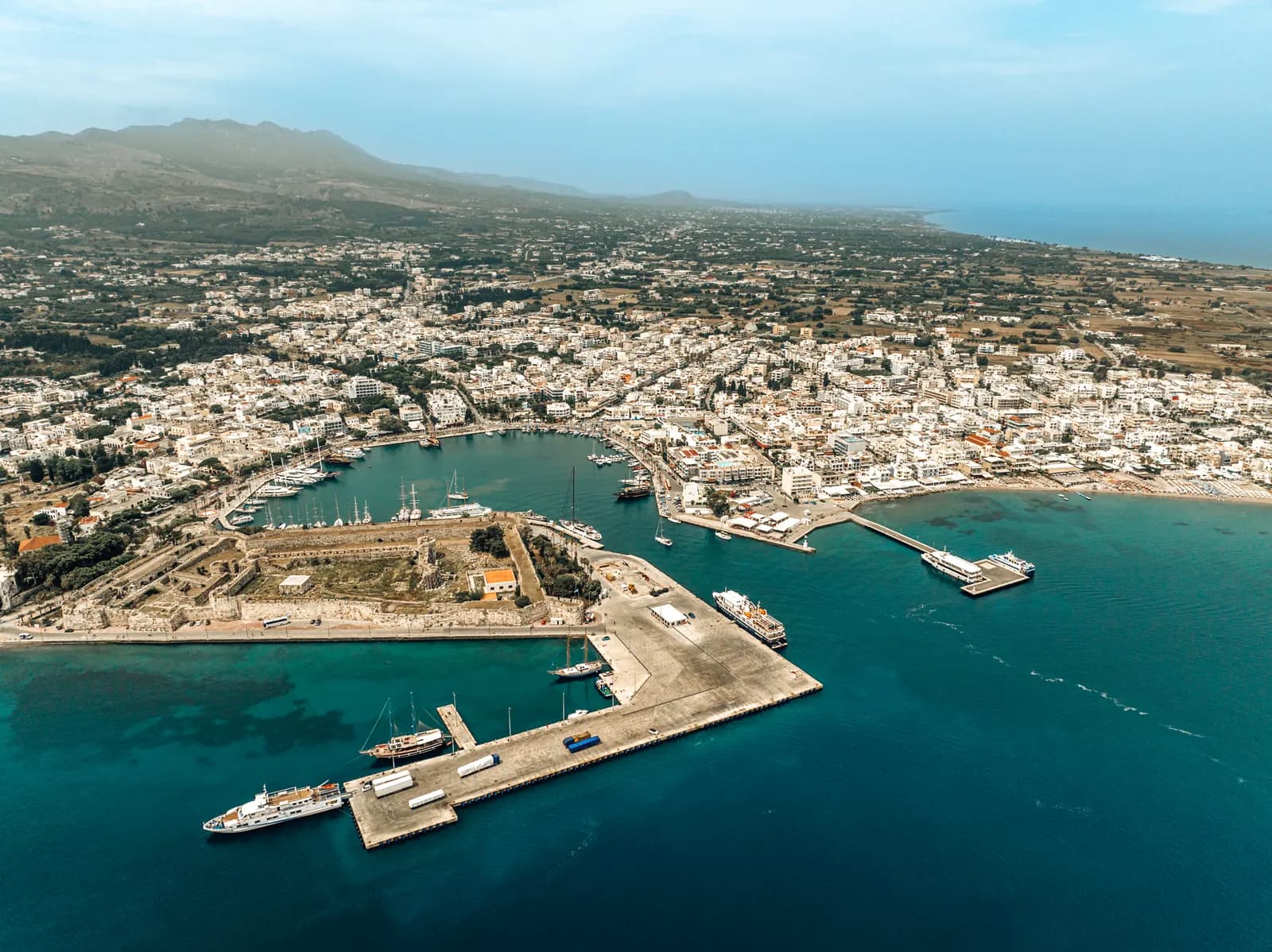 Aerial view of Kos Town, with the Neratzia castle and the harbour quays in front, white houses spreading inland and Mount Dikeos behind