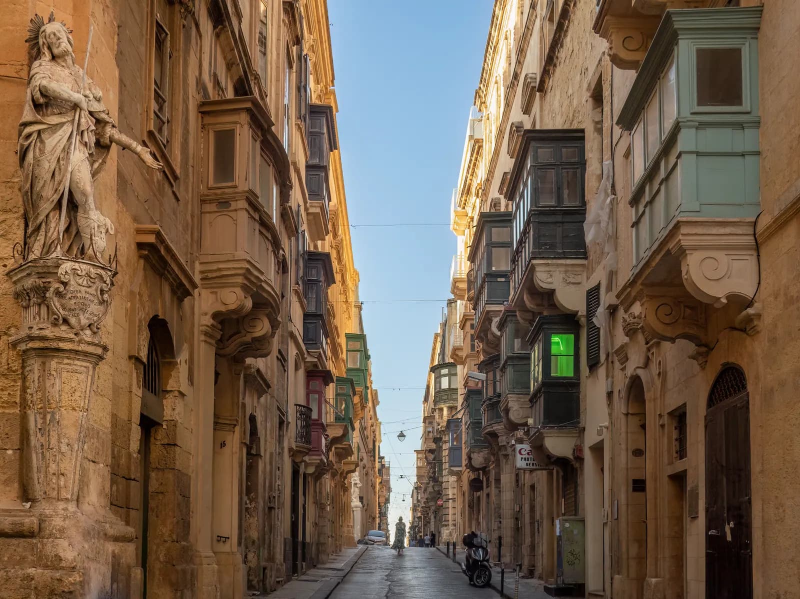 Saint Christopher Street in Valletta, a narrow street of limestone houses with enclosed wooden balconies and a statue of St Roque on the corner