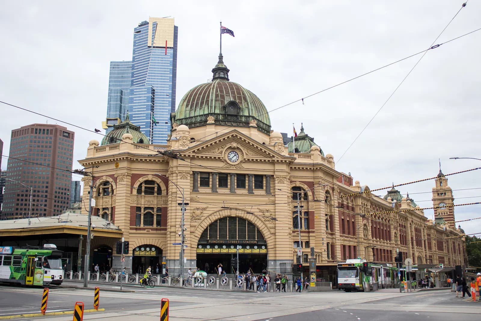 Flinders Street Station in Melbourne, with its green domes and clock, trams on the street in front and the Eureka Tower behind
