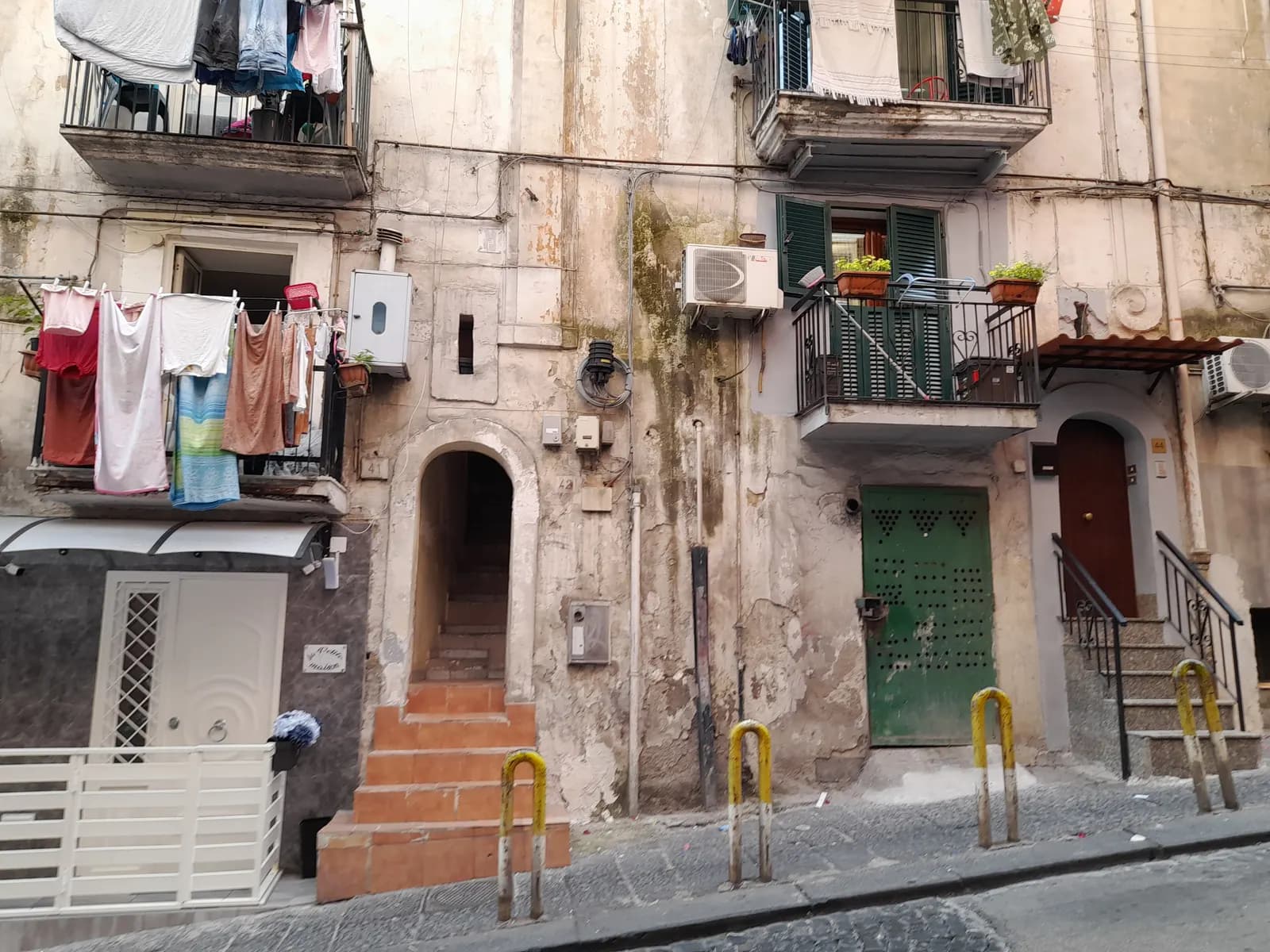 A street in the Quartieri Spagnoli with laundry on the balconies, a stairway doorway and a green door in a weathered facade.