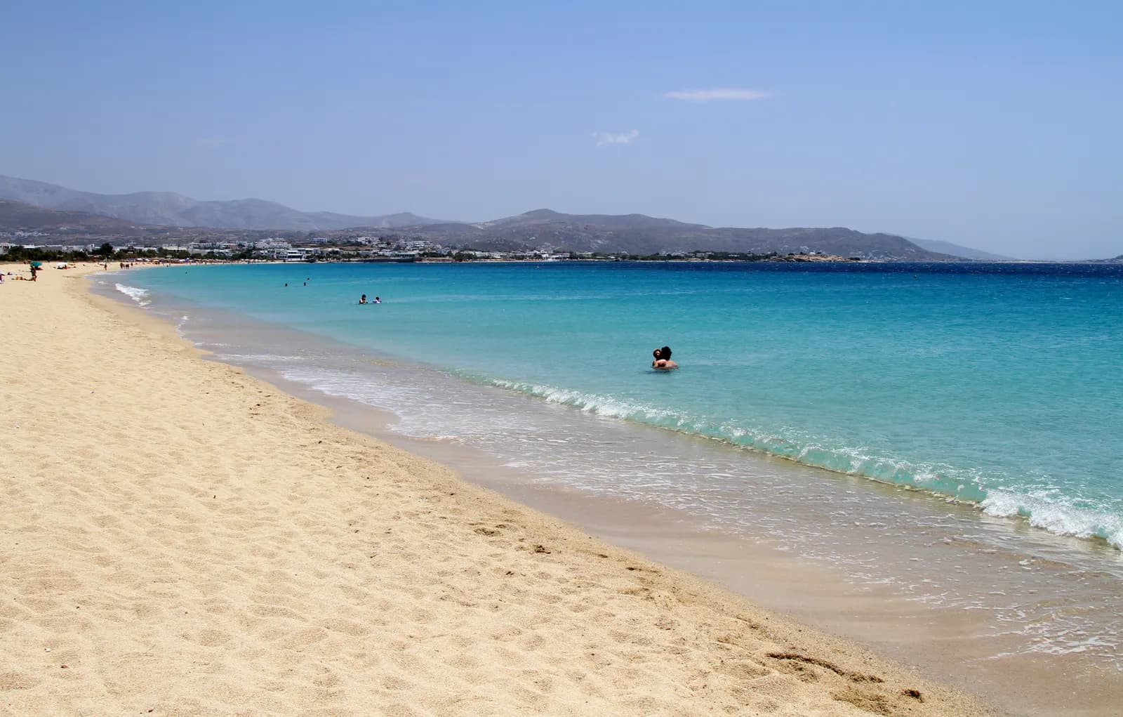 The long sandy beach of Agios Prokopios with shallow turquoise water and low hills along the coast