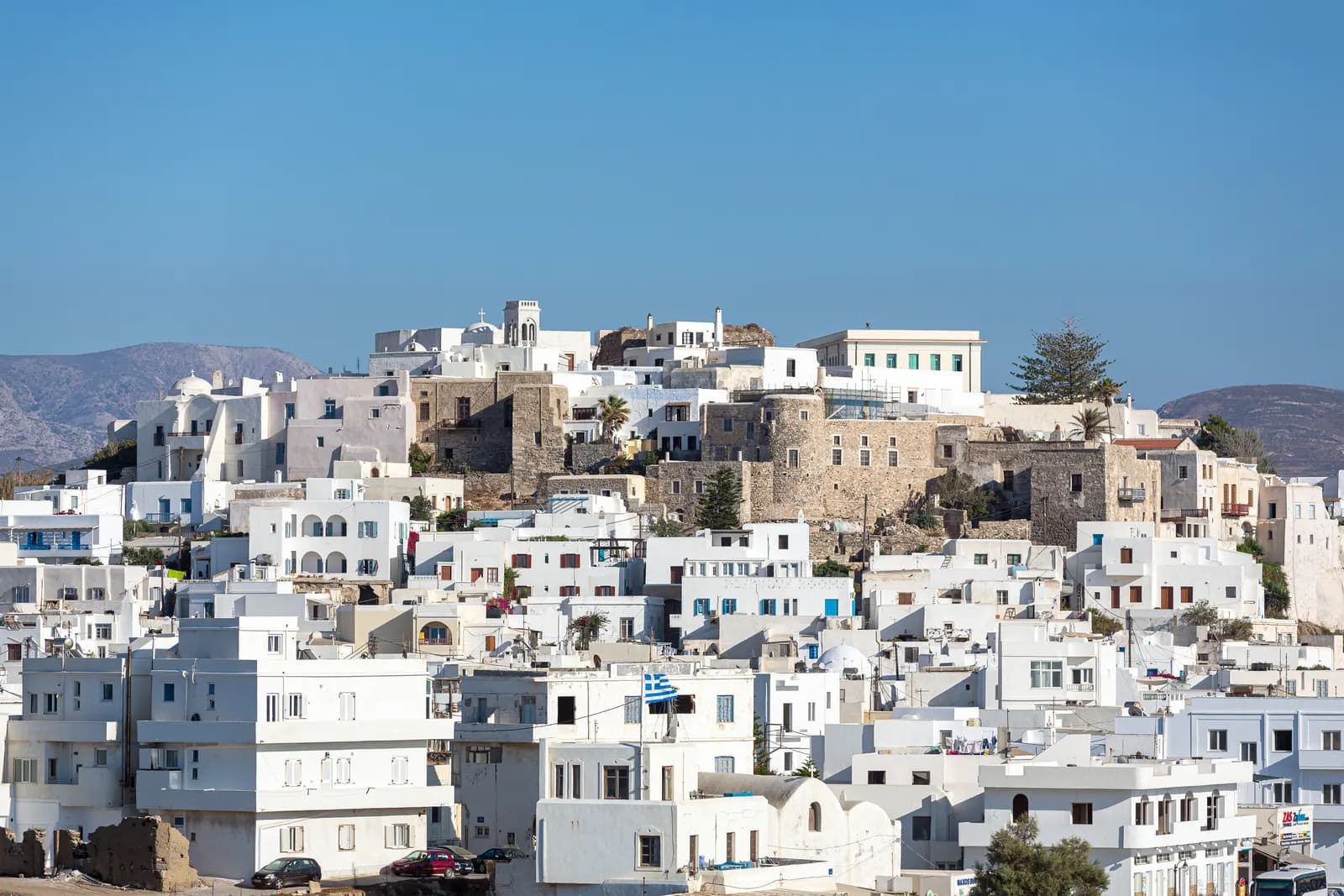 The white houses of Chora climbing the hill to the stone walls of the Kastro, with cars parked at the foot
