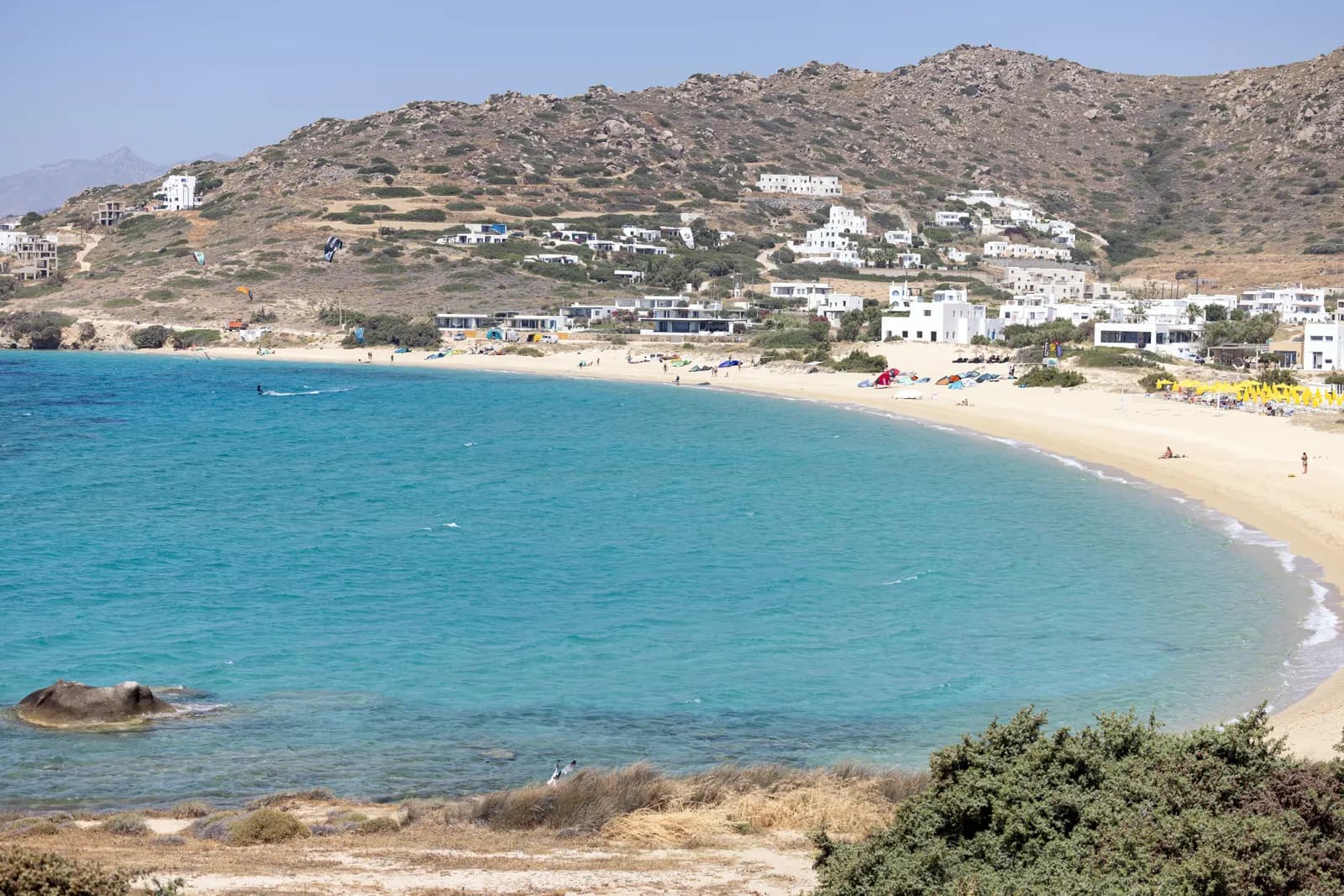 The curved sandy bay of Mikri Vigla with kitesurfers on the water and white houses on the hillside above