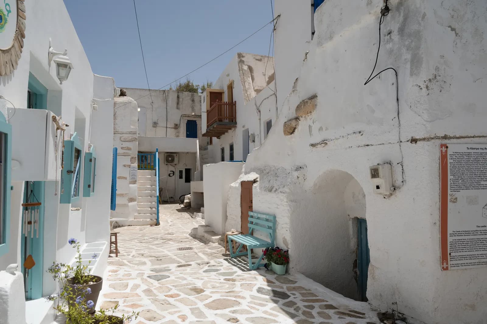A whitewashed lane with a blue bench and a stone paved floor inside the Kastro of Antiparos town