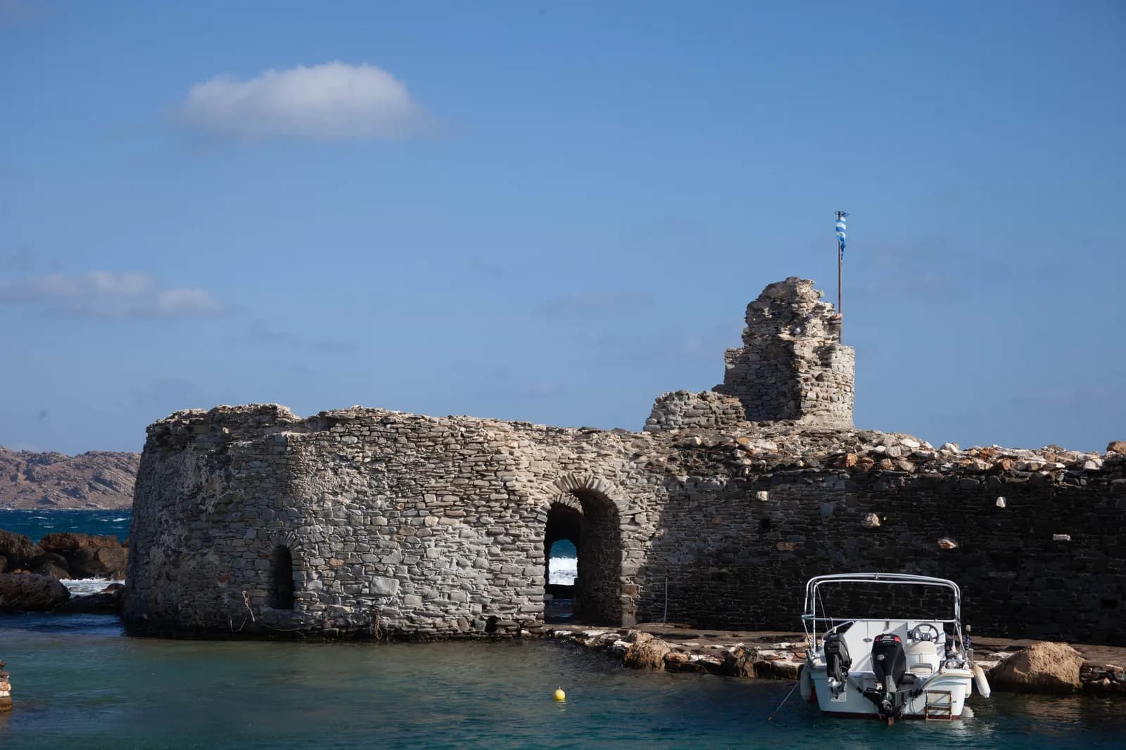 The stone ruin of the Venetian castle at the entrance to Naousa harbour, with a small motor boat tied up beside it