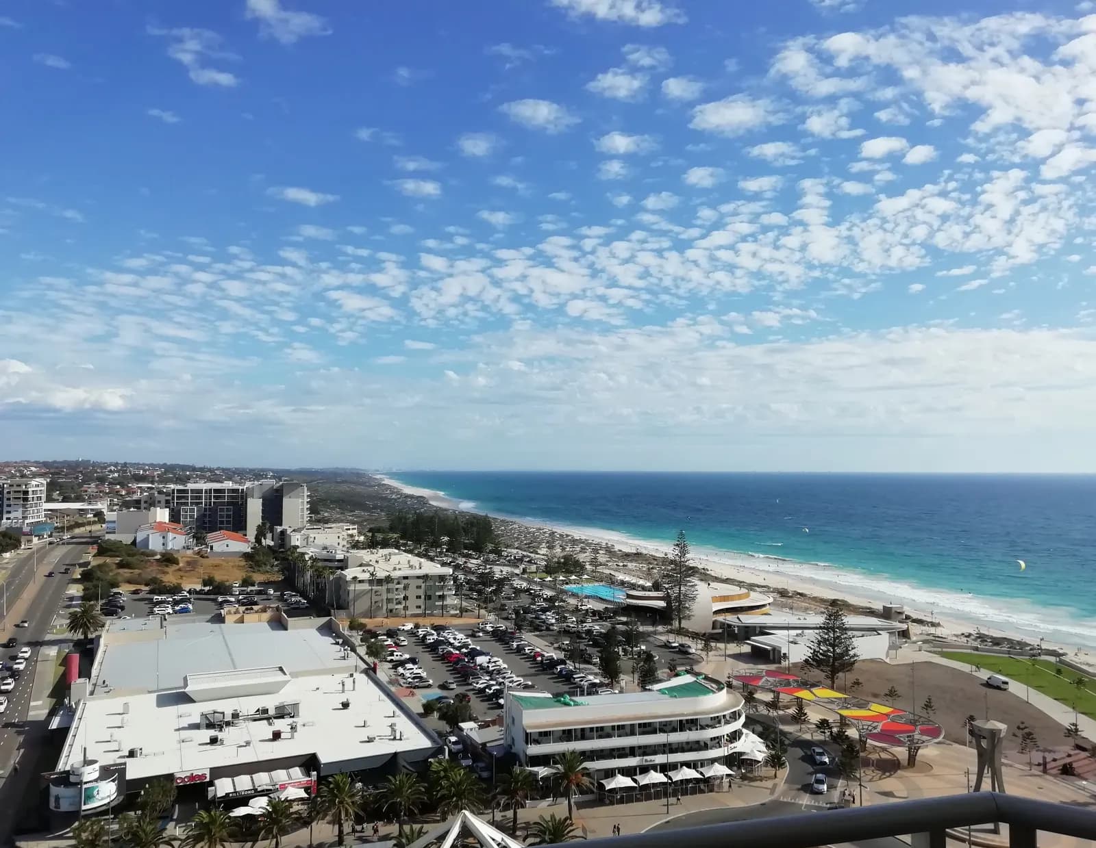 Scarborough seen from a hotel tower, with shops, large open-air car parks, a swimming pool by the beach and the sand running south along the ocean
