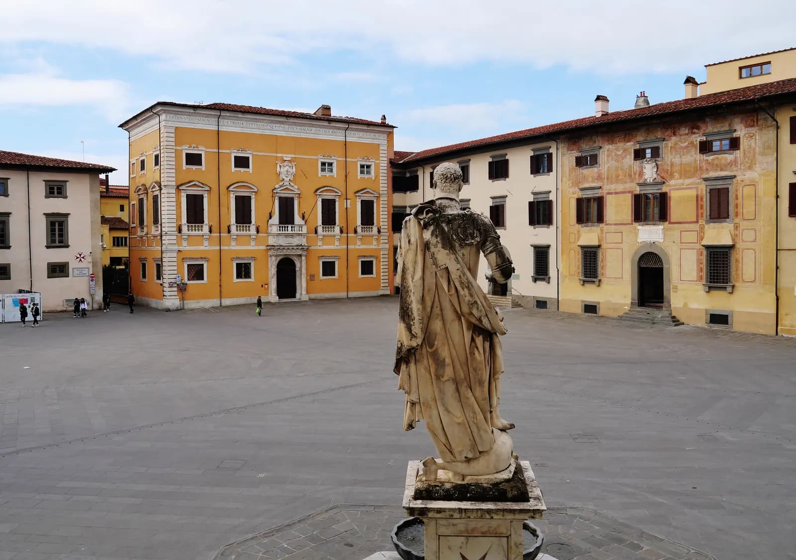 Piazza dei Cavalieri in Pisa, with a statue on a fountain in the foreground and painted palazzi around the square.
