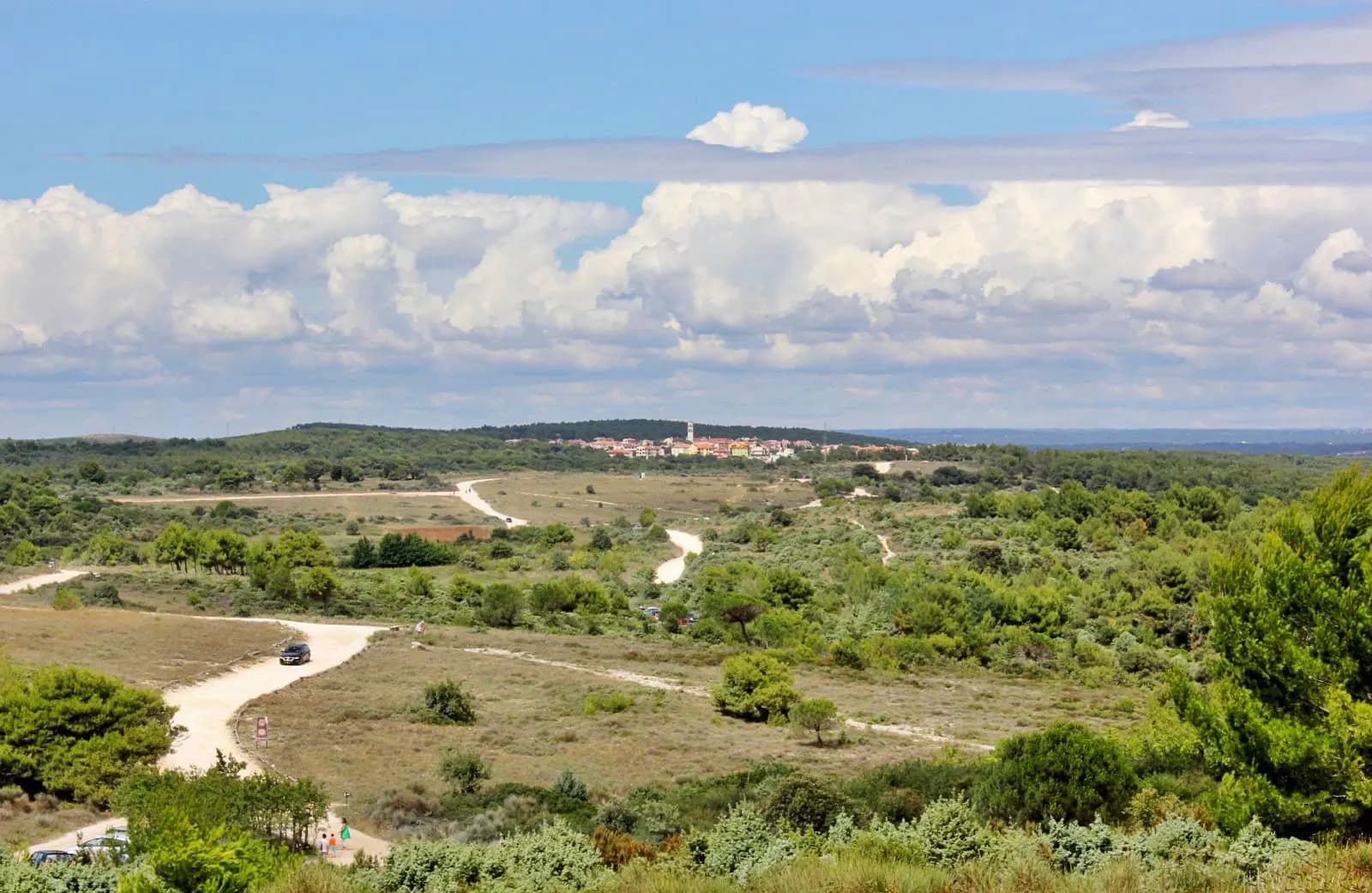 Gravel tracks through the scrub of Cape Kamenjak with a car on one of them and the village of Premantura on the horizon