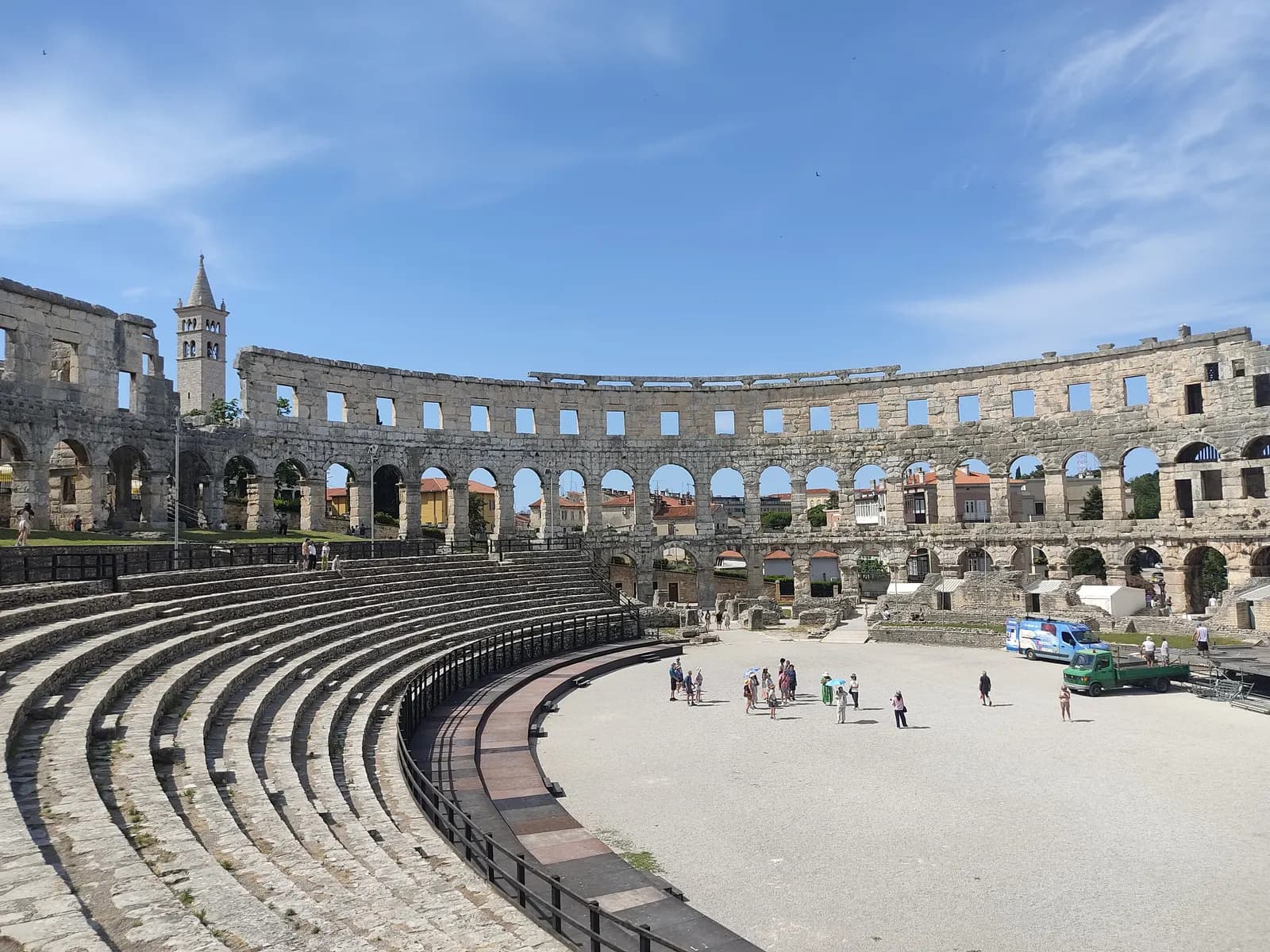 Inside the Roman amphitheatre in Pula, with stone seating, the arched outer wall and a church bell tower beyond it