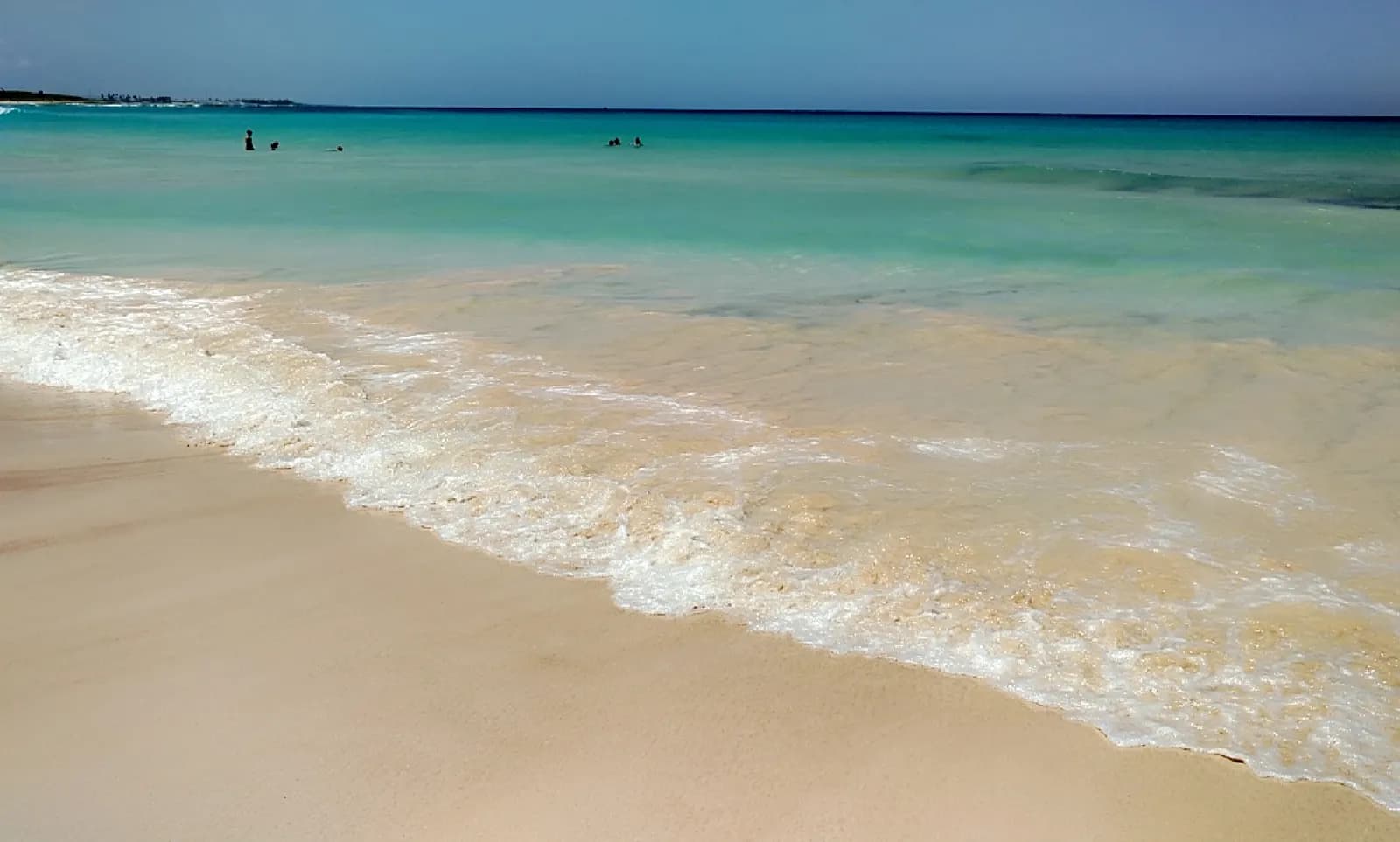 A wave washing onto the pale sand of Playa Macao, with turquoise water and a few swimmers further out