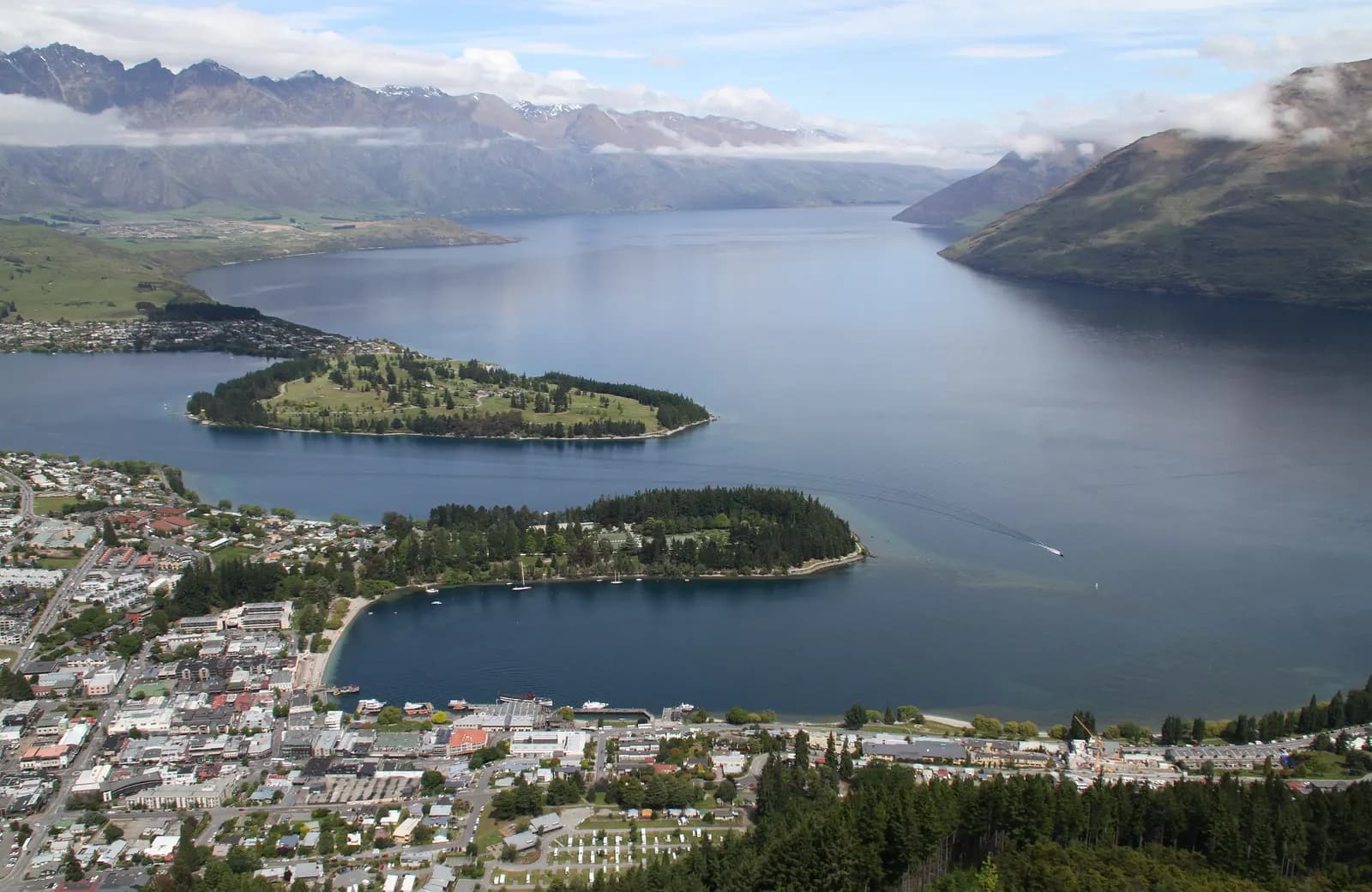 Queenstown's town centre curving around Queenstown Bay on Lake Wakatipu, seen from the hill above, with wooded peninsulas and mountains beyond