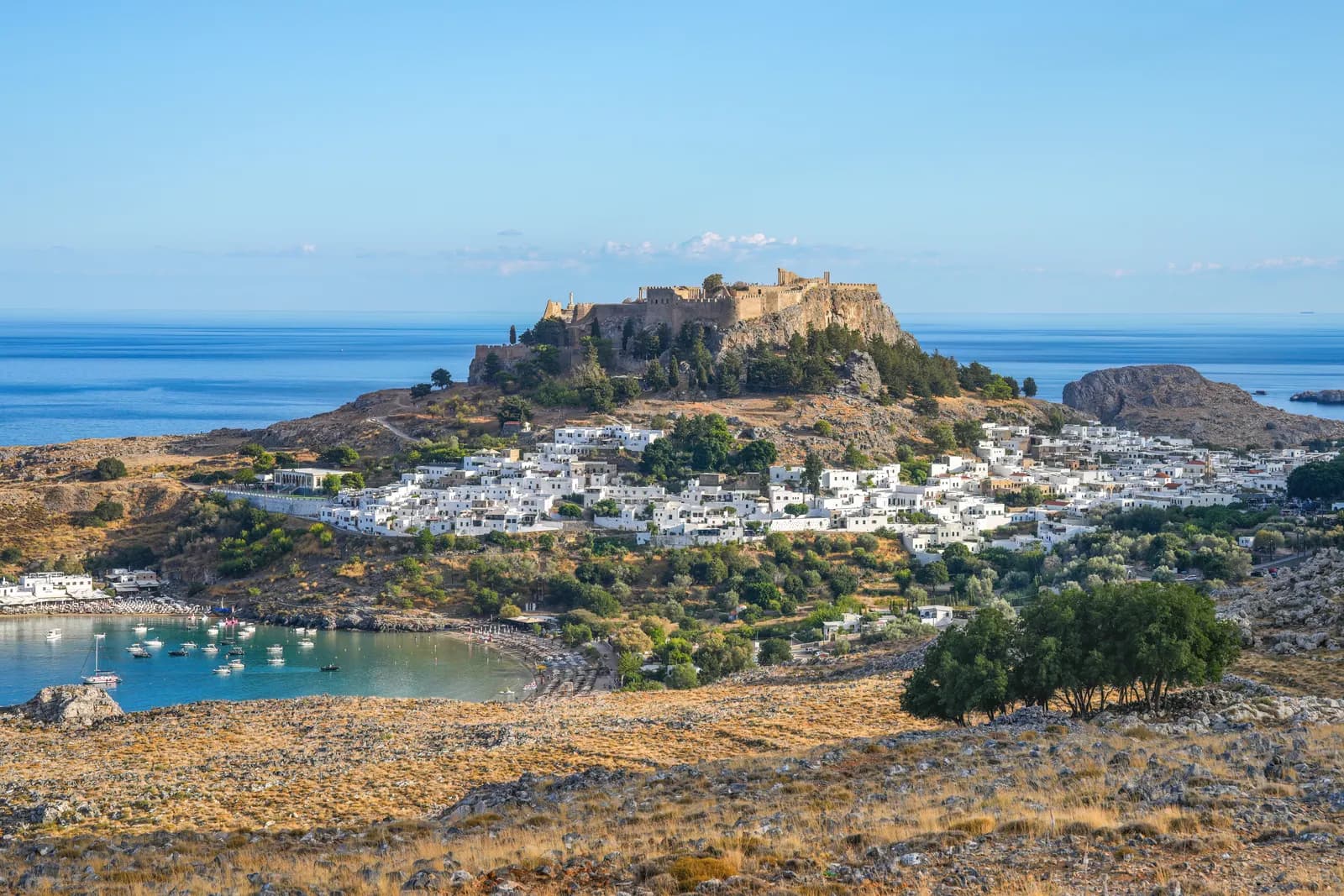 The acropolis of Lindos on its rock above the whitewashed village, with boats moored in the bay below and the open sea beyond
