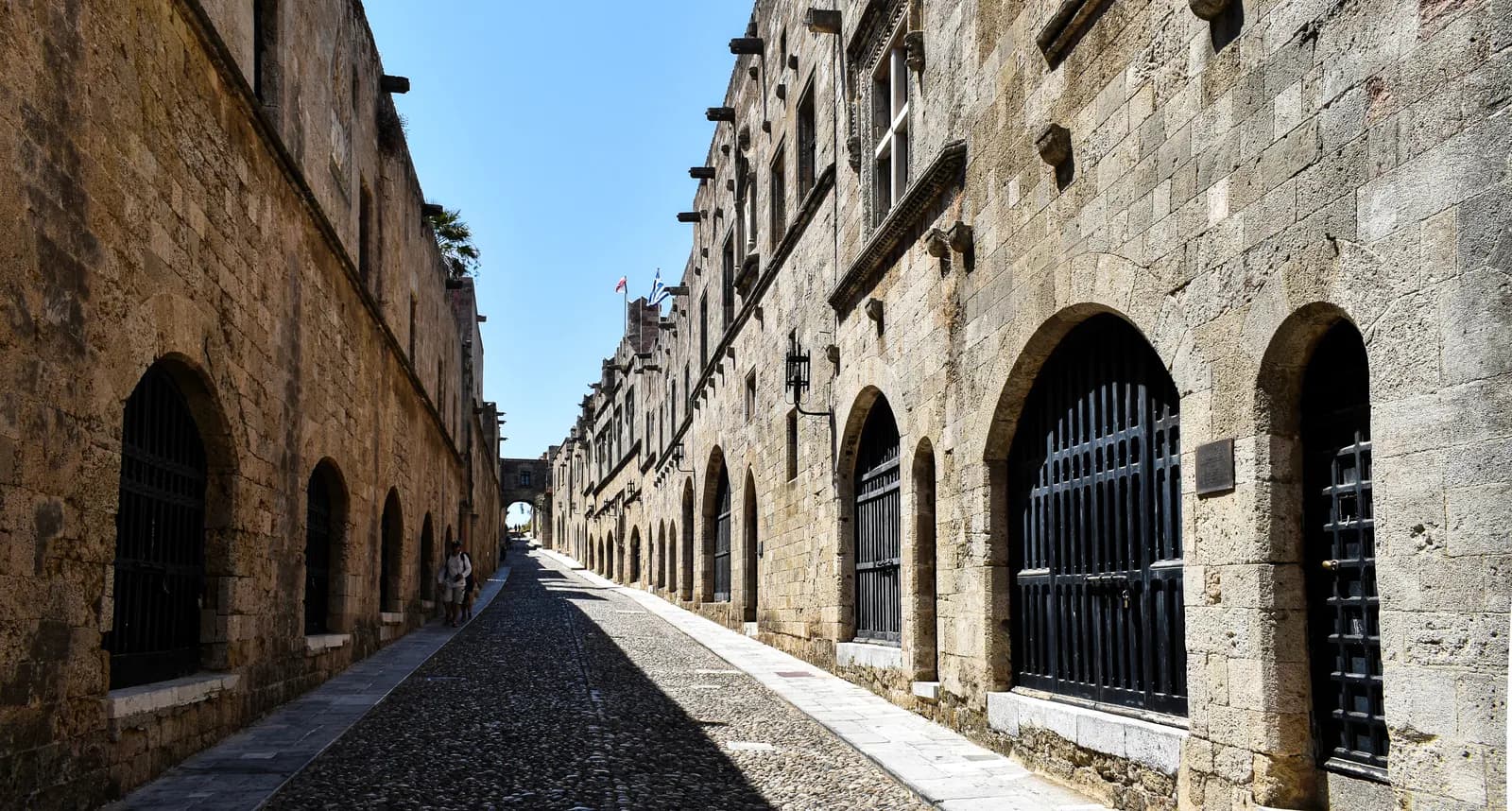 The Street of the Knights in the medieval Old Town of Rhodes, a cobbled lane between stone buildings with arched, barred doorways