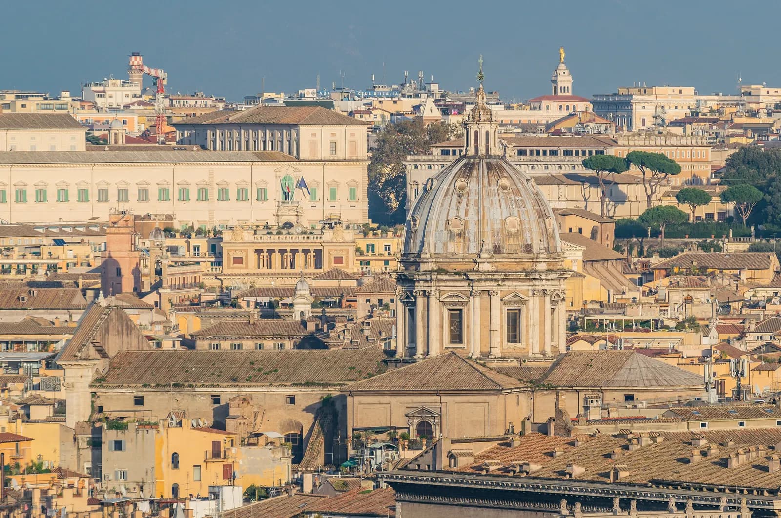 Rome's tiled roofs seen from the Janiculum, with the grey dome of Sant'Andrea della Valle and the Quirinal Palace behind it.