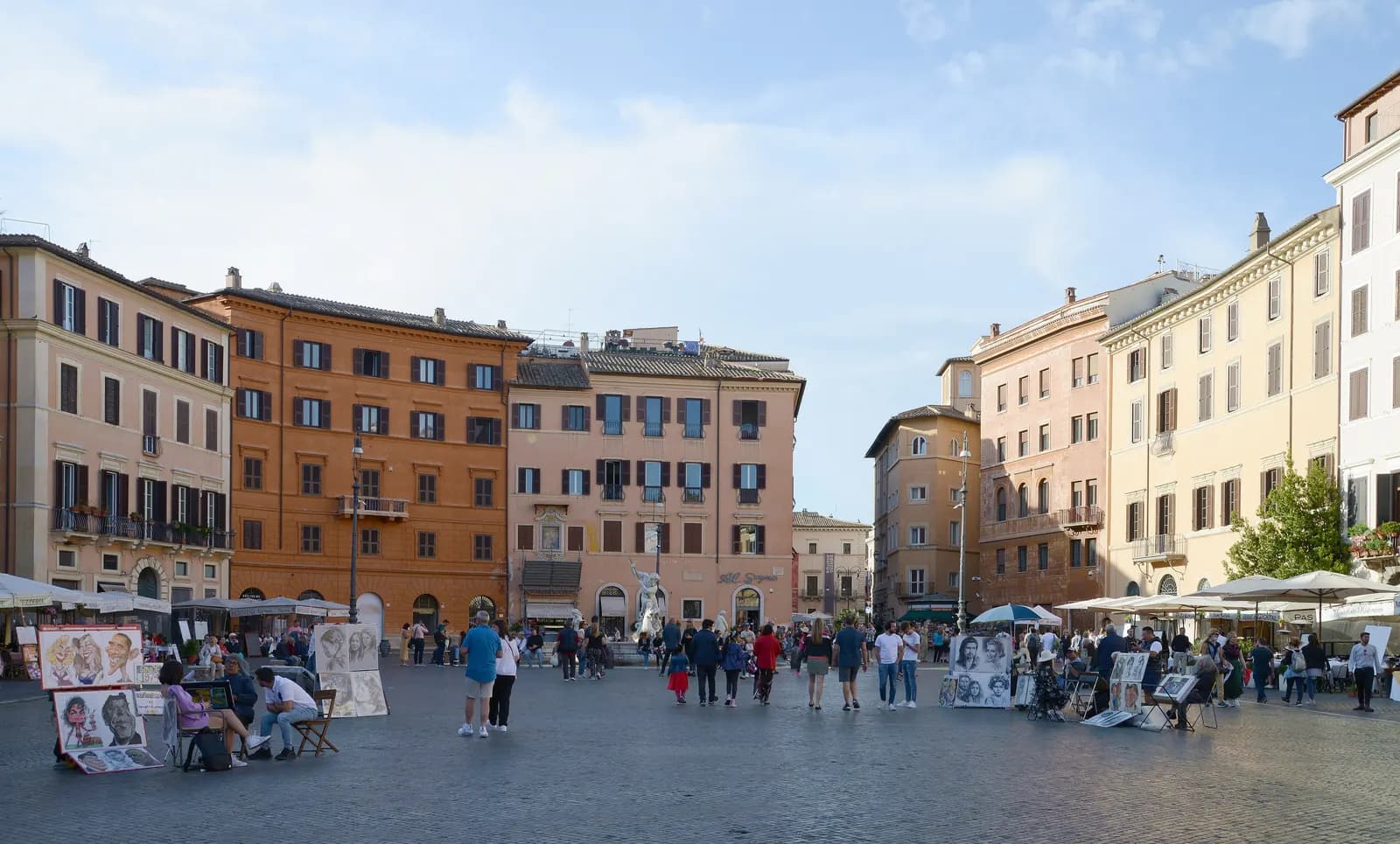 Piazza Navona on a sunny afternoon: ochre and pink palazzi, street artists' easels, café umbrellas and a fountain at the far end.