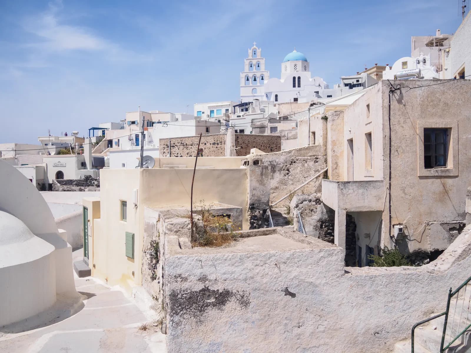 Old stone and whitewashed houses of Pyrgos climbing the hill to a church with a white bell tower and a blue dome