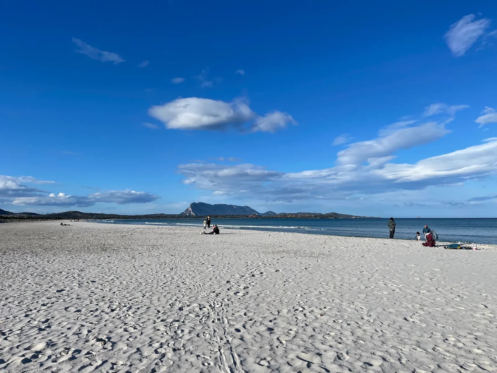 The white sand beach of La Cinta at San Teodoro under a blue sky, with the limestone mass of Tavolara island across the water