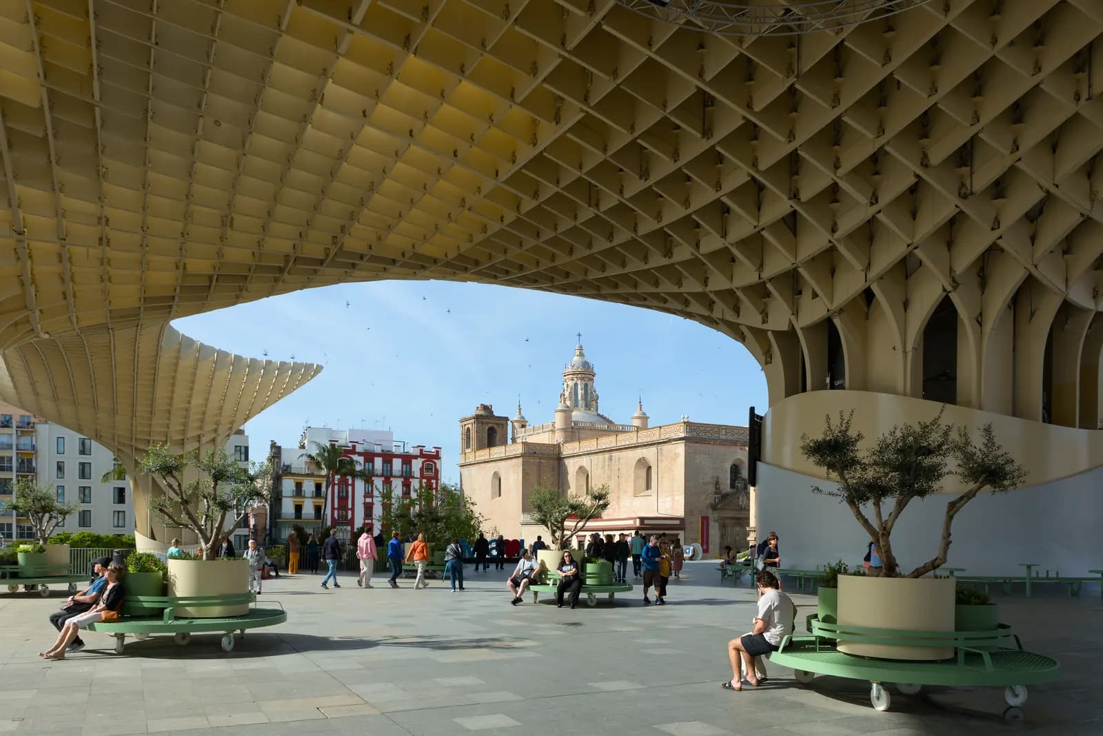 The wooden lattice of the Metropol Parasol framing the church of the Anunciación, with people on benches in the square below.