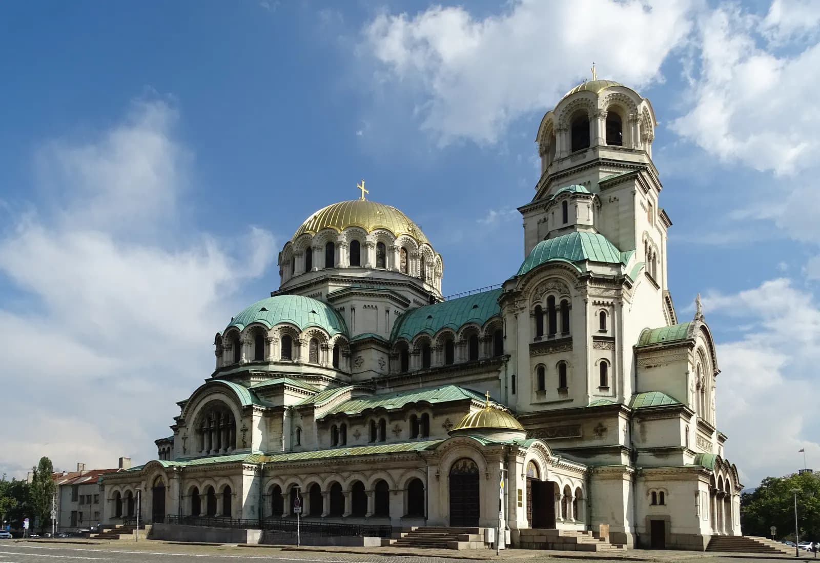 The Alexander Nevsky Cathedral in Sofia with its gilded main dome, green copper roofs and bell tower under a blue sky with white clouds