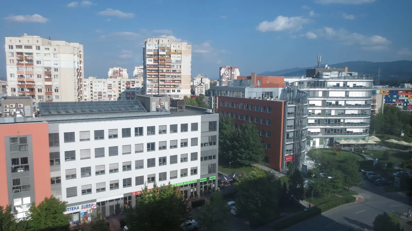 Tall apartment blocks of Mladost behind the office buildings and gardens of Business Park Sofia, with mountains on the horizon
