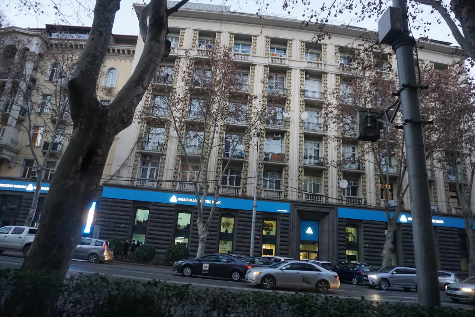 Apartment block with a bank on the ground floor and traffic along Ilia Chavchavadze Avenue in Vake, plane trees in winter