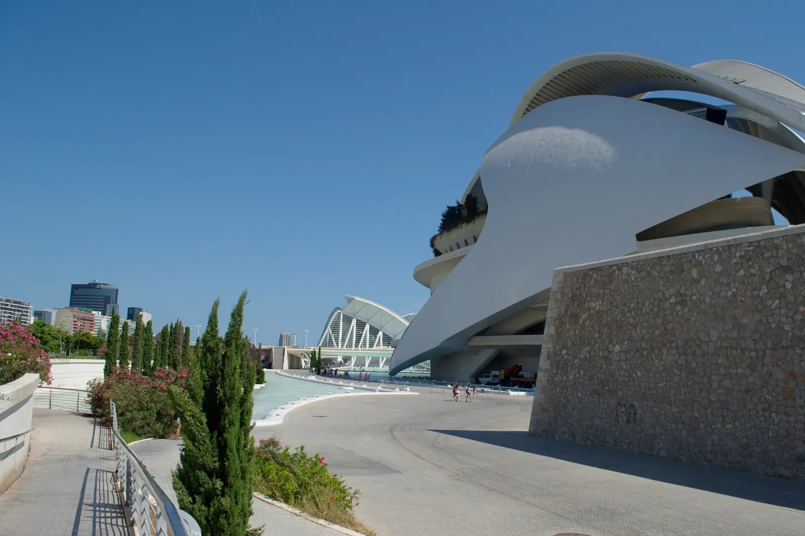 The curved white Palau de les Arts in the City of Arts and Sciences, with landscaped walkways under a blue sky.